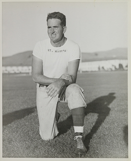 Portrait of Football Line Coach Tom Coll kneeling on a football field, undated