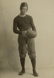 Portrait of Ted Brandon in football uniform holding a football, undated