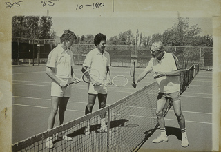 Two students with a tennis coach on a tennis court, 1979