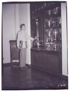 Unidentified person standing in front of a trophy case, undated